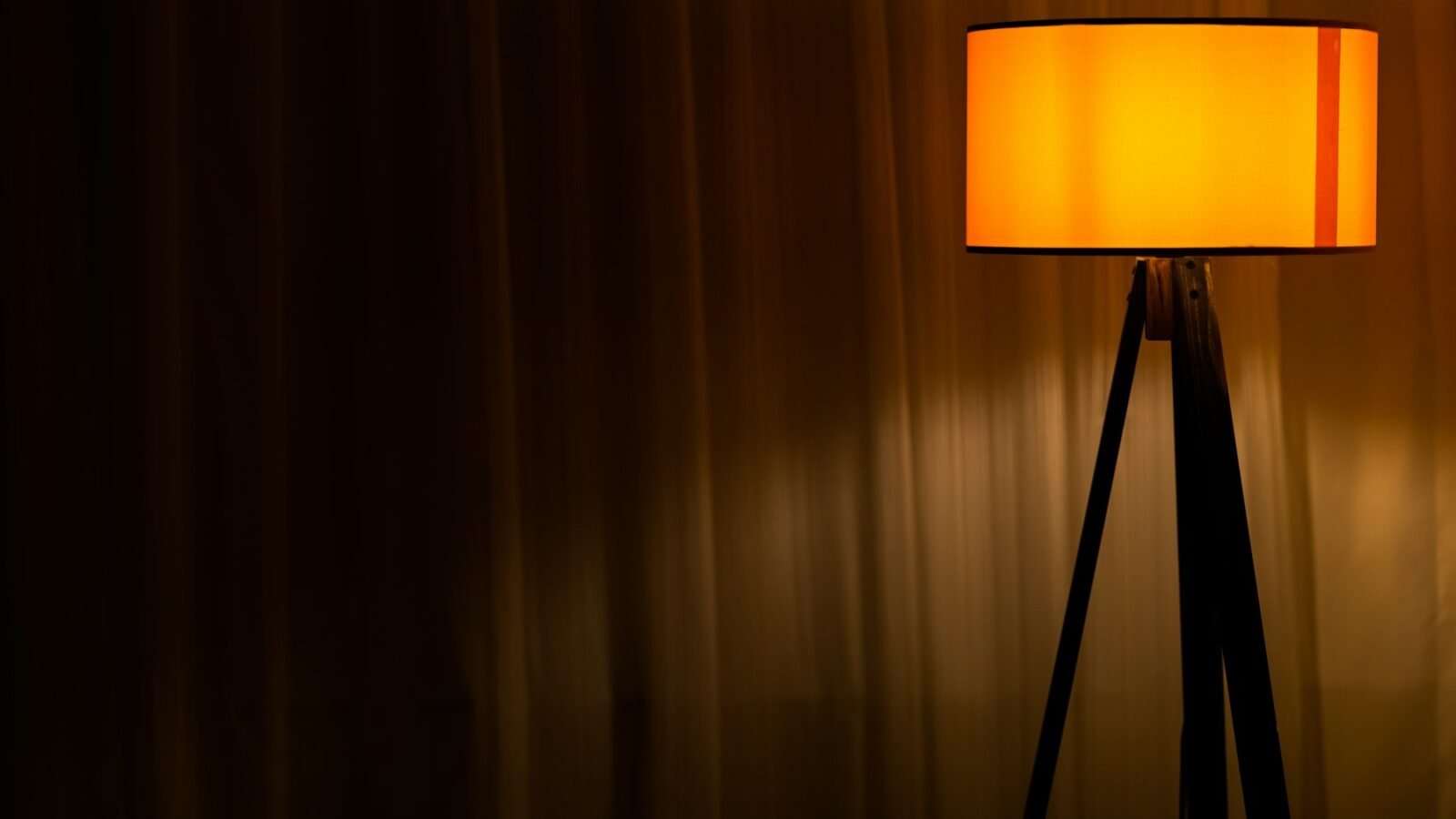 A brown table lamp switched on beside a curtain in a dim room