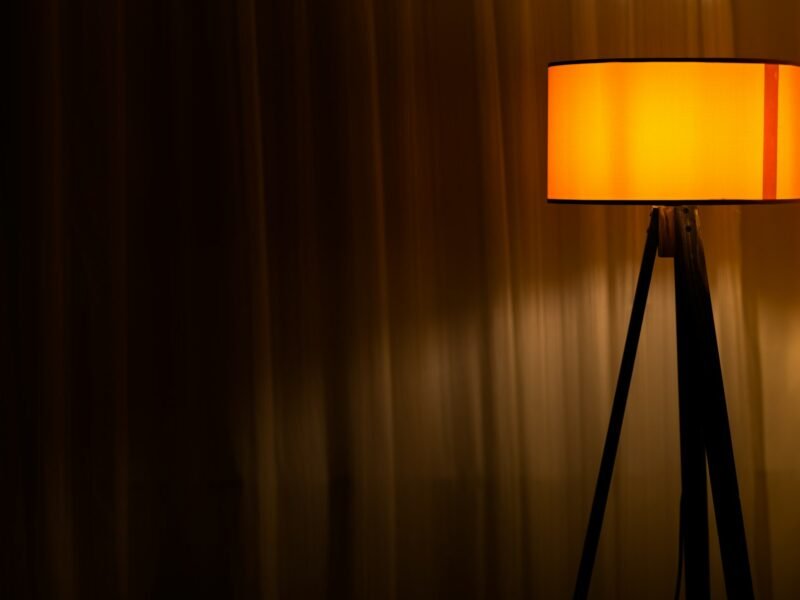 A brown table lamp switched on beside a curtain in a dim room